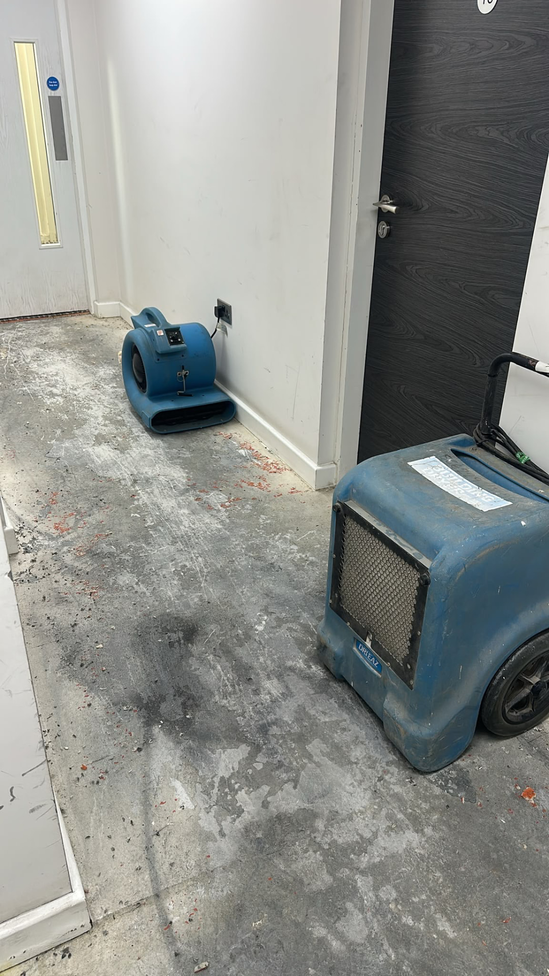 Dehumidifier and air mover drying a second-floor lobby with exposed floor