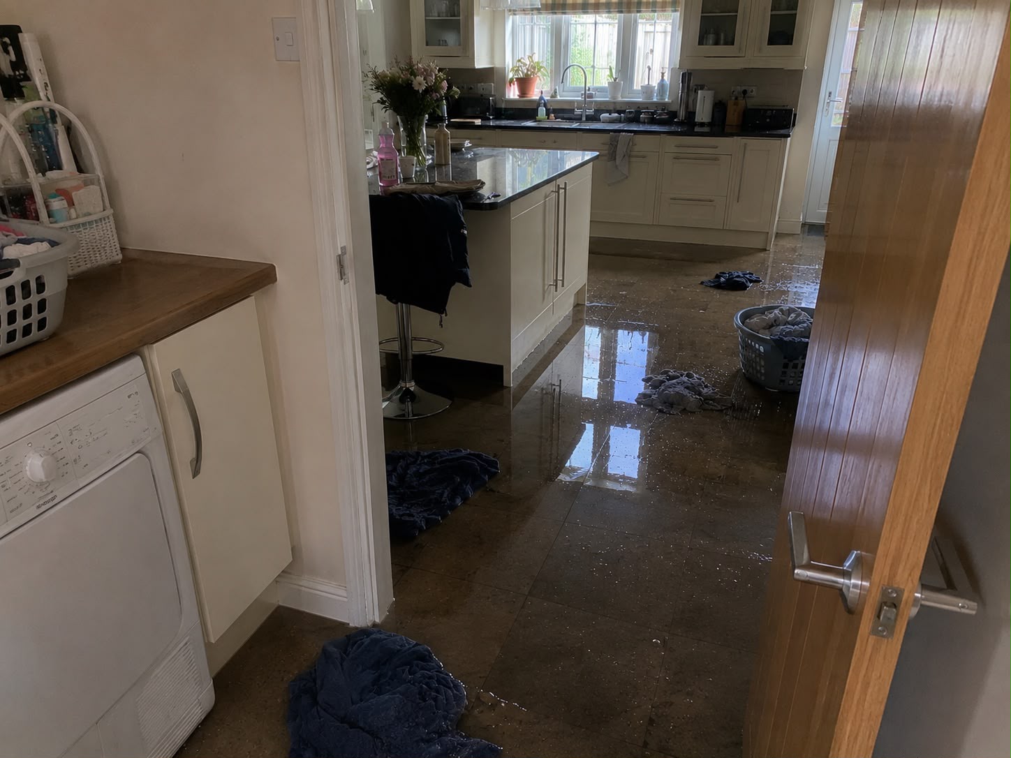 Standing water across kitchen tiled floor with wet towels used to contain the flood