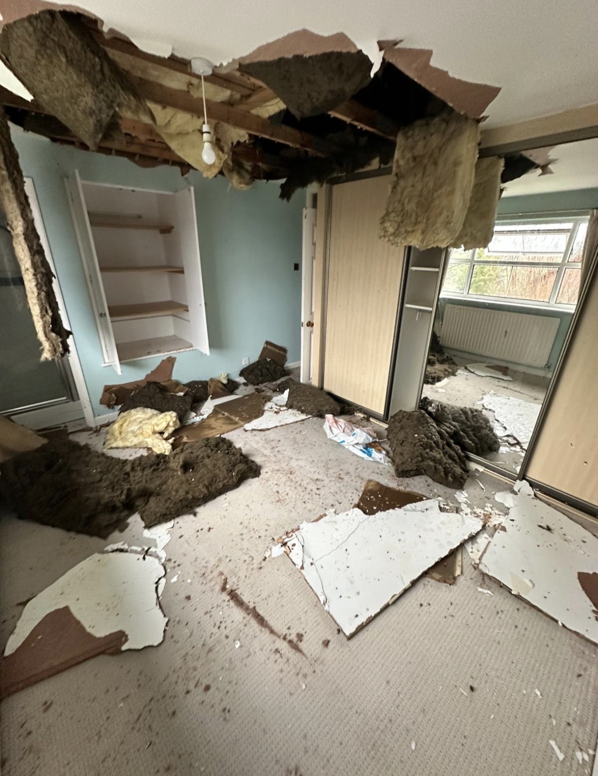 Main bedroom with water-damaged ceiling and exposed structure above the bed