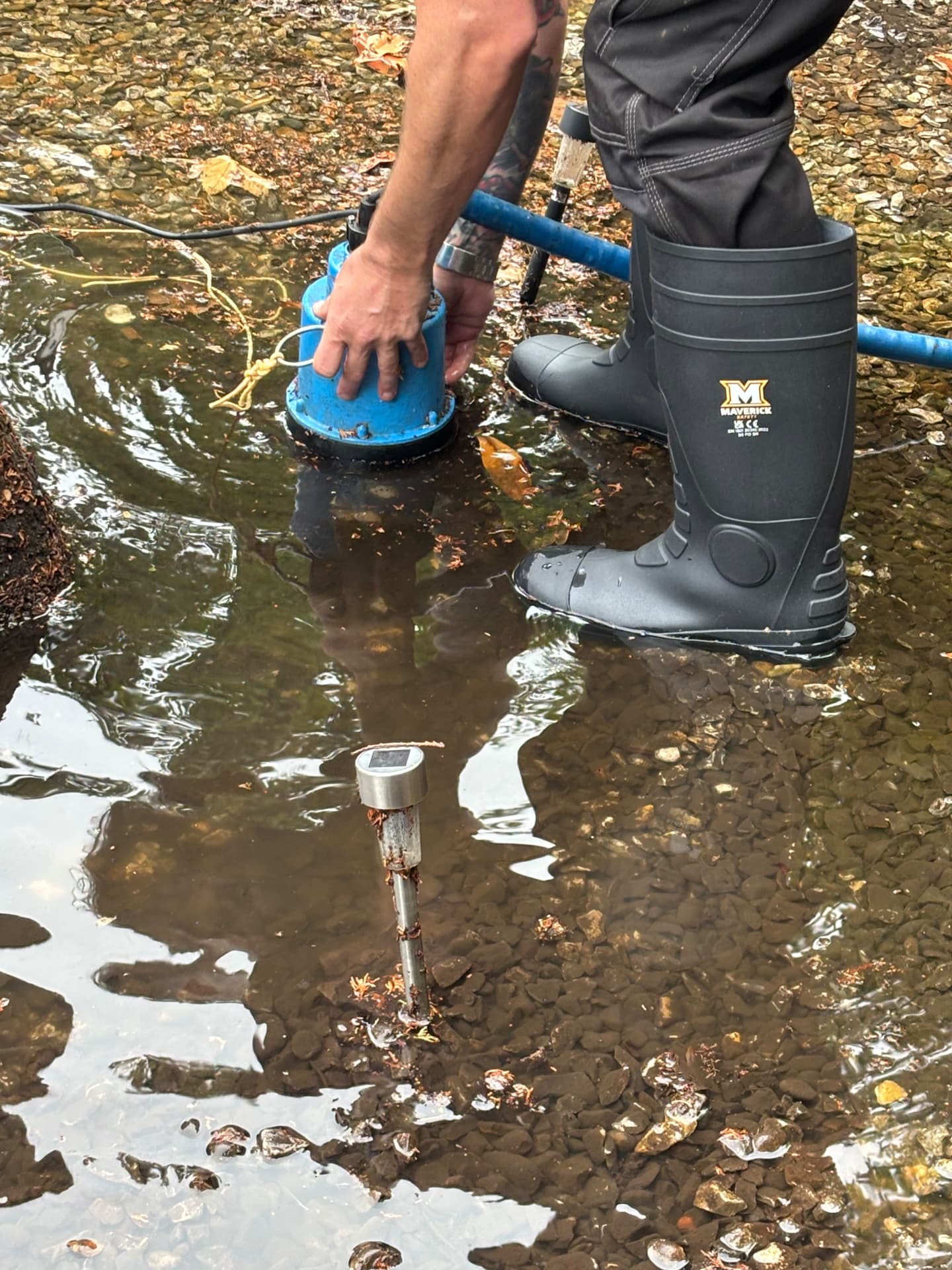 Close-up of a submersible pump being repositioned within standing water in a flooded garden
