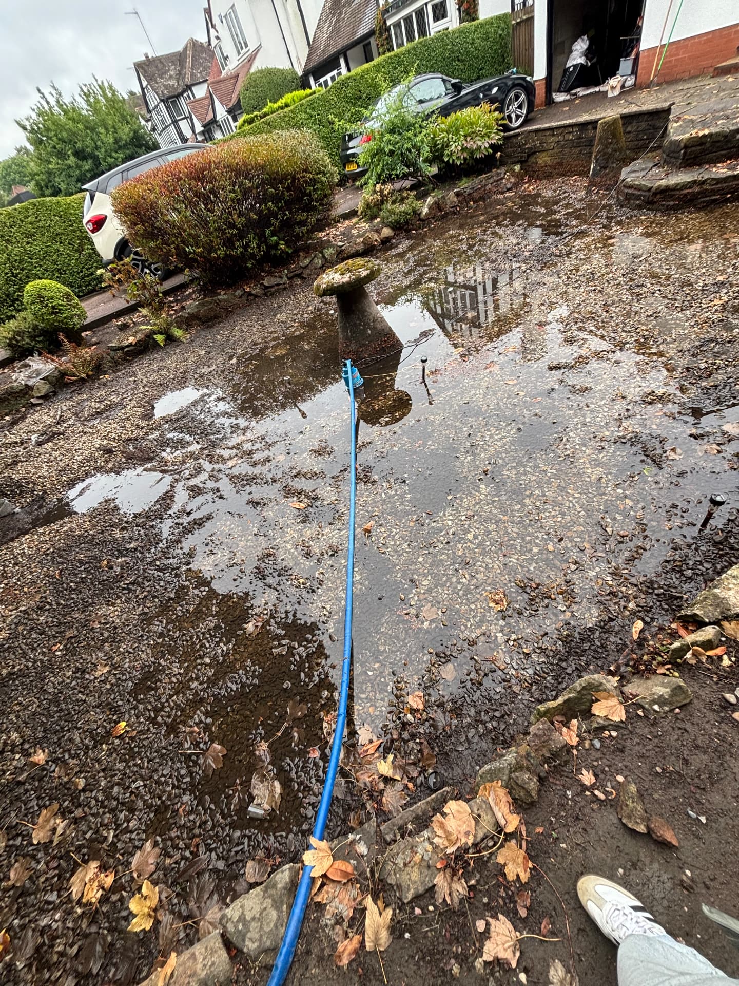 Standing water pooling across a gravelled front garden with a blue discharge hose running towards the pump position